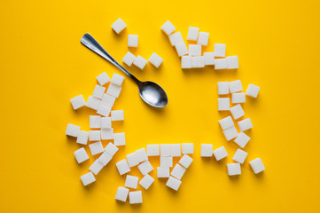 Refined sugar cubes and teaspoons shot on a yellow background. Background for sweets, and cutlery.