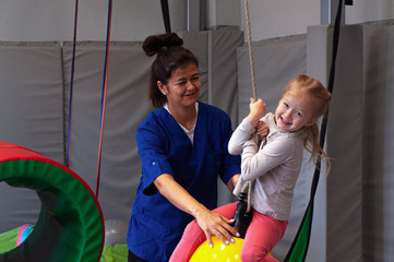 happy girl enjoying a sensory therapy on a swing with physiotherapist assistant