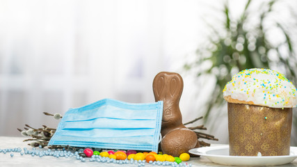 Easter cake, protective medical face mask and chocolate eggs and rabbit, close-up. Protection against viruses.