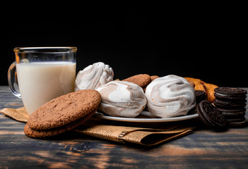 Milk with cookies, marshmallows and pastries on newsprint on a black background