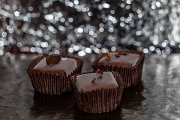 Immagine close-up ti tra cioccolatini assortiti appoggiati su piano scuro con sfondo argentato