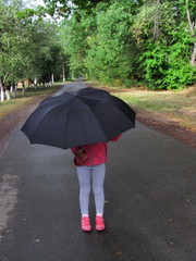 
A girl stands in the middle of the road under a black umbrella