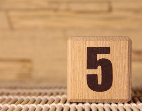 A wooden cube with the number five on a beige background.