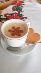 cup of coffee with milk and a drawing with cinnamon next to a cookie