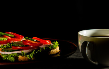 delicious sandwiches with ham, lettuce, cucumber, tomato and a Cup of coffee on a dark background.