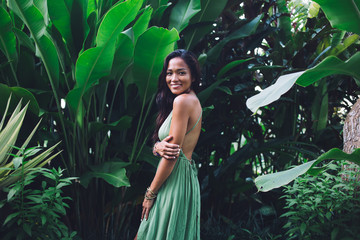 Smiling Asian woman in romantic dress standing against lush foliage