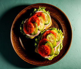 delicious sandwiches with ham, tomato, cucumber and lettuce on a green background