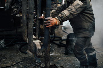Work driller in red uniform, in helmet and goggles. He uses a hydraulic wrench to screw drill pipes to lower them into an oil well and continue drilling it. The concept of a working person.