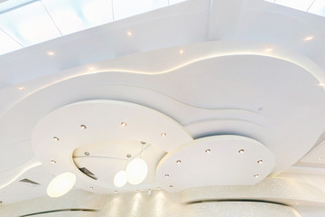 looking up on suspended ceiling with halogen spots lamps and drywall construction in empty room in apartment or house. Stretch ceiling white and complex shape. - obrazy, fototapety, plakaty