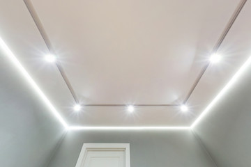 looking up on suspended ceiling with halogen spots lamps and drywall construction in empty room in apartment or house. Stretch ceiling white and complex shape.