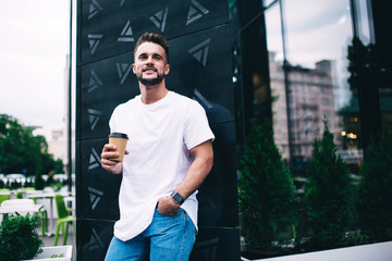 Happy man standing with coffee cup near modern office building