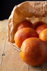 Macro closeup of blood oranges in paper bag, with selective focus, on rustic wooden board and black...