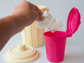 A hand is littering a used and folded surgical mask in the pink container. The used masks used as a tool to protect from COVID-19 epidemic after that the masks can become an infectious waste.