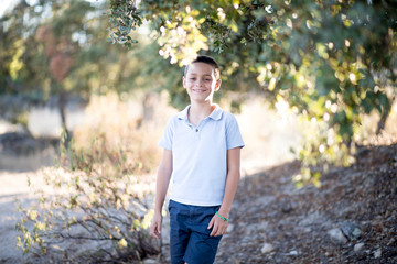 Handsome boy smiling and standing under tree in nature during golden hour.