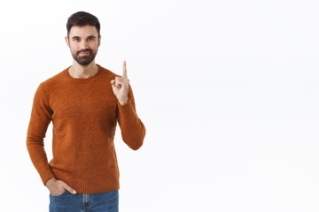 Portrait of confident smart, bearded man pointing finger up, showing way to advertisement, smiling,...