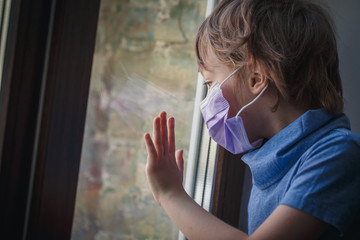 a little boy looks out the window in a medical mask
