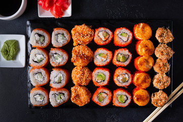 set of Japanese rolls Philadelphia with salmon, California with caviar, baked with cheese and eel, wasabi, pickled ginger, soy sauce on a black background, top view,