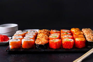 set of Japanese rolls Philadelphia with salmon, California with caviar, baked with cheese and eel, wasabi, pickled ginger, soy sauce on a black ,  lots of sushi