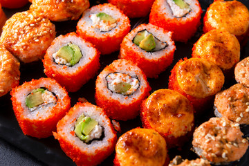many sushi , set of Japanese rolls  California with caviar,   Philadelphia with salmon, baked with cheese and eel, on a black  close up