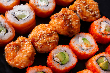 many sushi , set of  baked with  eel , cheese ,   Japanese rolls  Philadelphia with salmon,  California with caviar,   on a black
