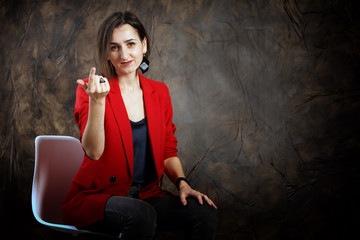Attractive woman in a red jacket sitting against a dark wall. Young mysterious girl. Dark tones. Copy space
