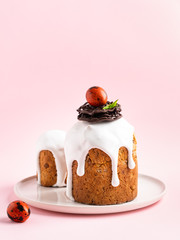 Easter cake with white glossy frosting decorated with chocolate nest, painted colorful quail eggs in it and green leaves. Pink background. Copy space. Elegant spring and easter celebration decor.