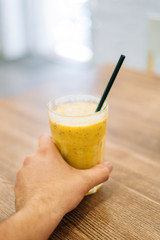 A male hand holds a glass of banana and berry smoothies. Glass of yellow smoothie on the table.