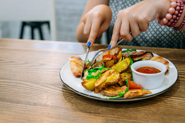Woman tastes chicken in bacon with baked potatoes . Restaurant food, knife and fork