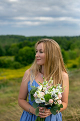 Naklejka na ściany i meble vertical close-up portrait of a beautiful thirty-five year old blonde with a bouquet against the backdrop of a summer landscape