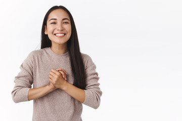 Grateful happy, smiling east-asian woman with long dark hair, clasp hands together pleased and delighted, thanking help, invite guest and grinning friendly, receive charming gift from secret santa