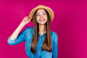joyful girl in a hat and denim shirt joyfully smiles at the camera on a pink background