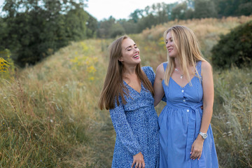 horizontal closeup portrait of two cheerful young women on the background of a grassy slope in the countryside