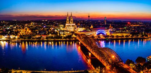 Fototapeta premium Cologne, Germany: Beautiful panoramic aerial night landscape of the gothic catholic Cologne cathedral, Hohenzollern Bridge and the River Rhine at sunset, golden hour and blue hour.