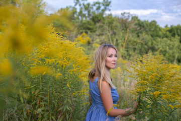 horizontal closeup portrait of a charming blonde on a background of a blooming field, sky and trees
