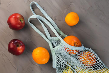 Different fruits, bananas, apples, oranges, in the blue mash or string bag, shopper on the grey textured abstract background, zero waste concept, no plastic, reusable, eco friendly philosophy