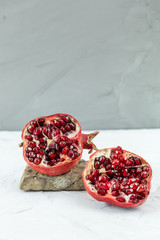 Halved red ripe pomegranate on the little grey stone isolated on light textured background, natural...