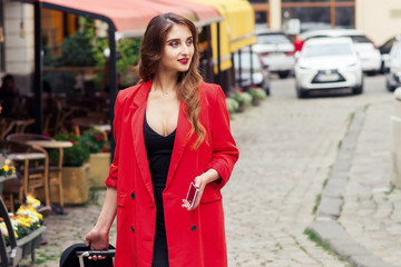 Traveling business woman wearing red cloak walks down city street.