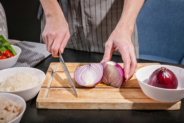 Female graceful hands cut red onion on a cutting board. Chef at work in the kitchen