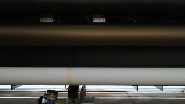 Details of a moving print head. Massive machinery. Professional printing facility, big vinyl rolls, ready for market. Glossy, matte, ecological materials used for commercial billboards and press.