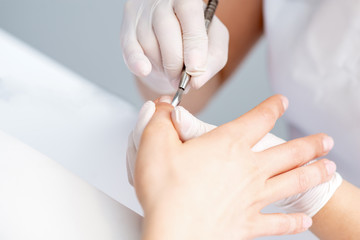 Close up manicure master hand cleaning cuticle with professional manicure metal stick tool.