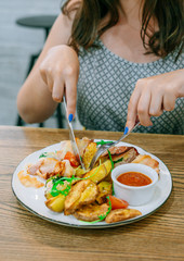 Woman in cafe tastes chicken in bacon and sauce. Meat, potatoes and sauce on a white plate. The knife and fork cut the dish