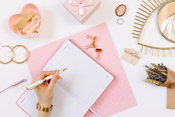 Left-hander girl keeps a diary and planning a day on stylish workplace. Female hand write in pink notebook. Women blog concept with pink notebook and golden watch. Flat lay style. 