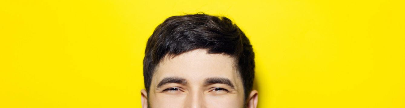 Close-up of smiling eyes of asian guy, panoramic portrait on yellow background.