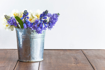 Bouquet of blue hyacinths and white daffodils in rustic bucket on wooden table and white background. Space for text
