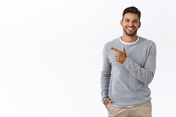 Handsome carefree bearded caucasian man in grey sweater, pointing left, discuss product, smiling as talking to you with friendly expression, showing around, introduce promo banner, white background - Powered by Adobe