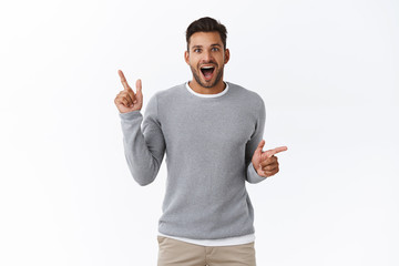 Cheerful excited guy spot interesting promo and share with us. Smiling handsome man pointing sideways as shopping in store with variety choices, open mouth fascinated look amused and happy