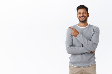 Joyful good-looking friendly nice bearded guy in grey sweater, laughing from funny joke or advertisement, smiling carefree and delighted, chatting with friend and pointing left, white background