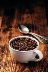 Roasted coffee beans in cup over wooden surface