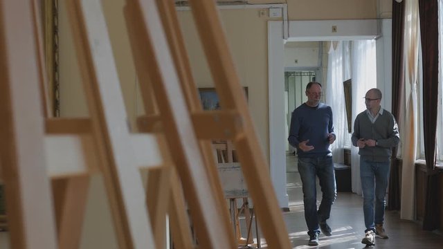 Two men walk through the halls of the art gallery and talk about art