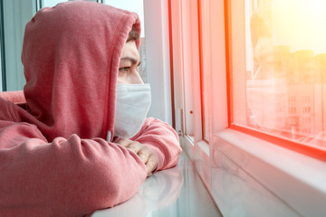 young man in a protective mask at home outside the window. A call for self-isolation due to a...